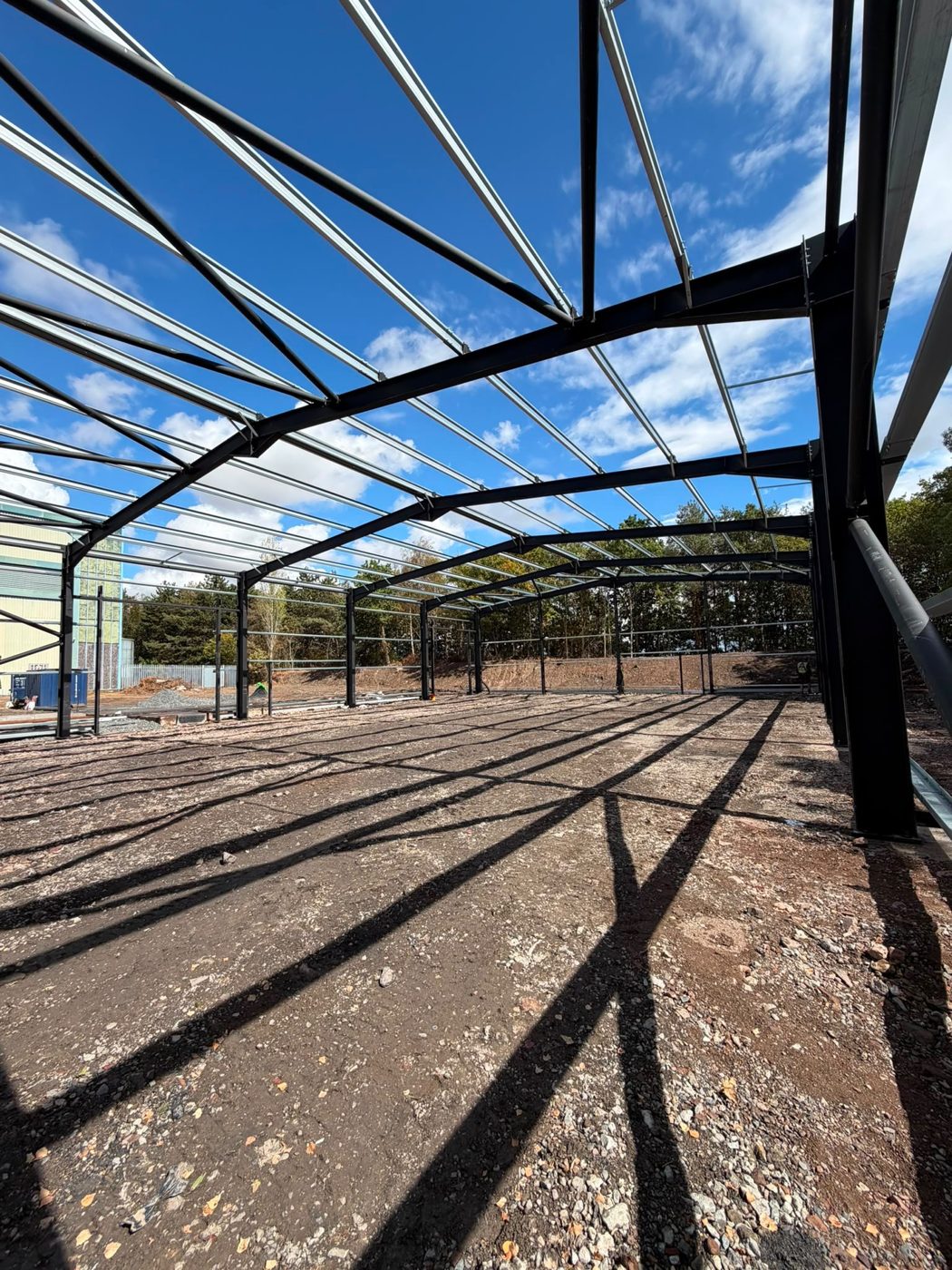 Looking up at the curved steel roof frame against a blue sky, from inside the part-built building