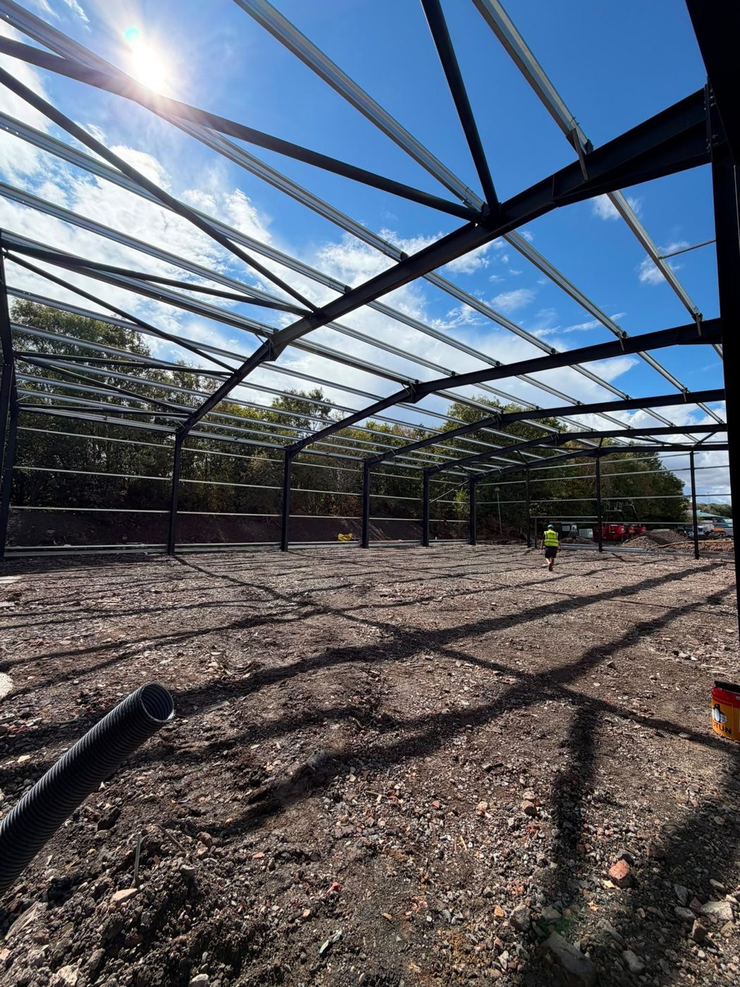 Inside the steel frame with the sun low over the roof beams and a site worker in the distance